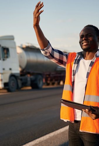 Showing the way. Black man is standing on the road with truck on it Showing the way. Black man is standing on the road with truck on it.